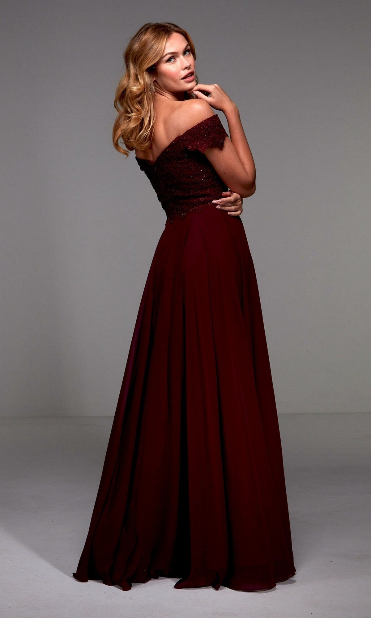 A woman wearing the Alyce 27510 long formal dress stands in a plain studio, facing away and looking back over her shoulder.